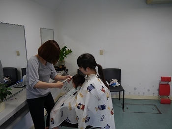 美容師が女性に抱っこされた赤ちゃんの髪を切っている