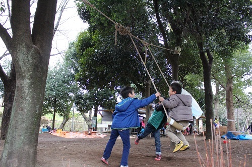 木の間に渡されたロープのブランコで遊ぶ子供たちの様子